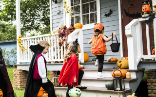 Children trick-or-treating at a porch decorated with pumpkins.