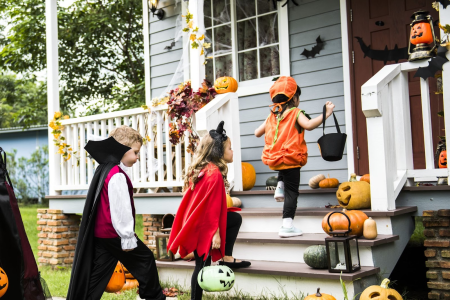 Children trick-or-treating at a porch decorated with pumpkins.