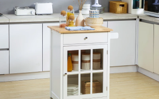 White kitchen cart with wooden top, open drawer, glass jars, and baskets in a bright kitchen.