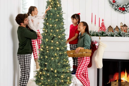 Family decorating tall pre-lit Christmas tree with warm lights near fireplace.