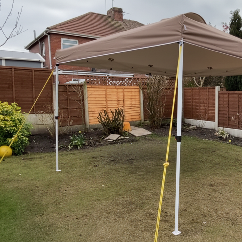 Brown canopy tent anchored with yellow ropes in backyard.