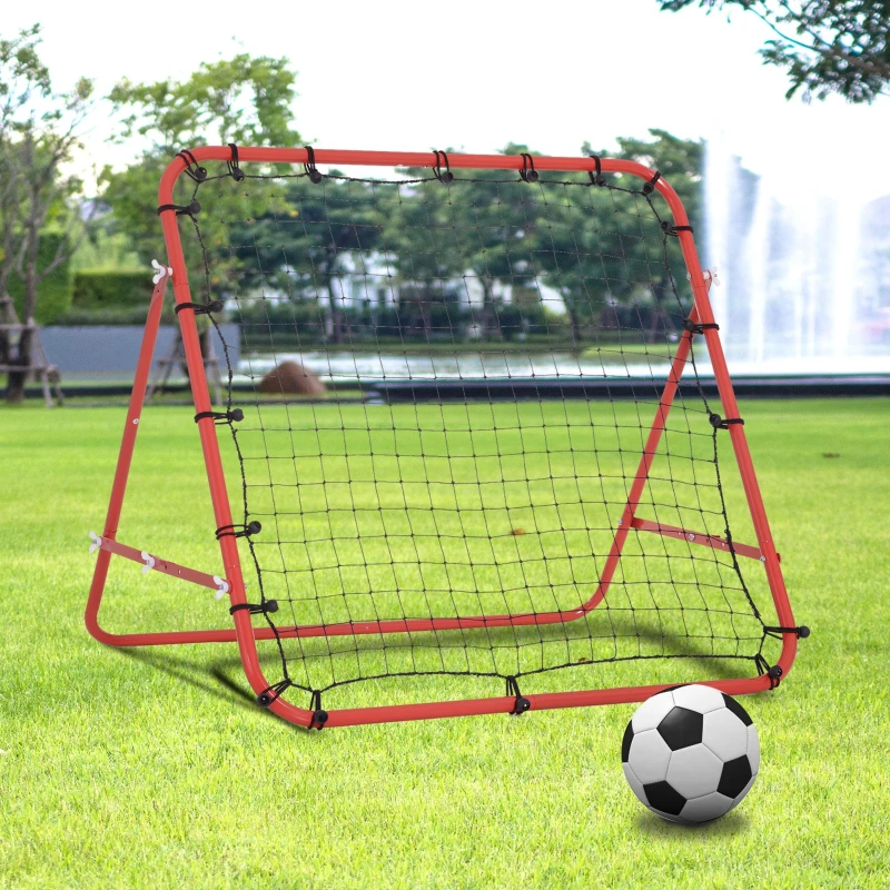 Red rebounder net with soccer ball on green grass near fountain.