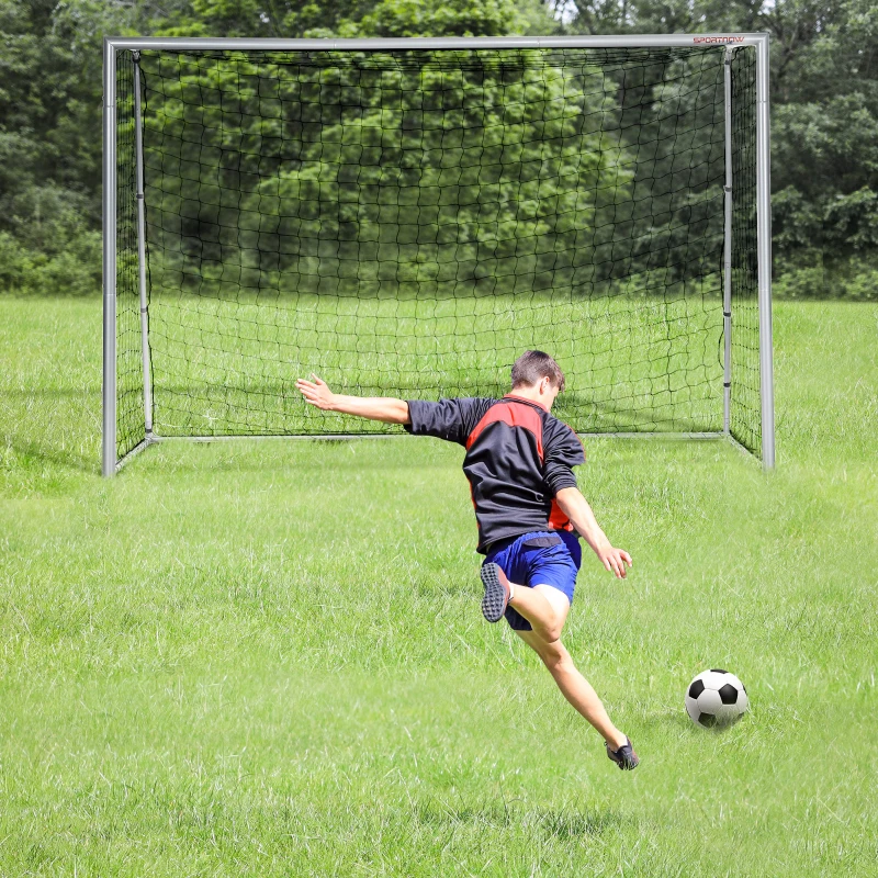 Boy kicking soccer ball toward large goal net on grassy field.