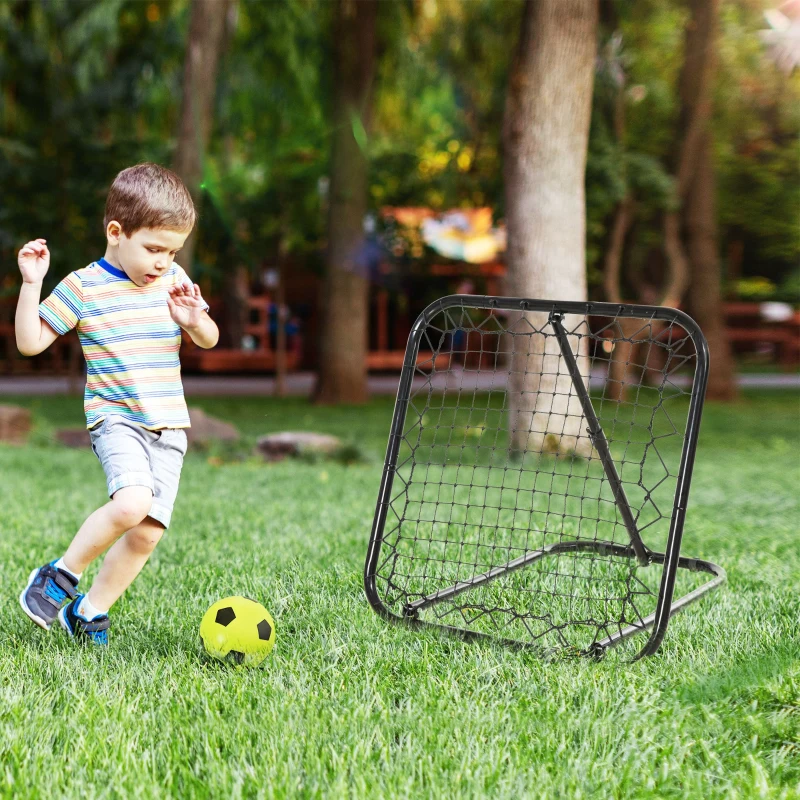 Small child kicking ball toward black rebounder net in park.