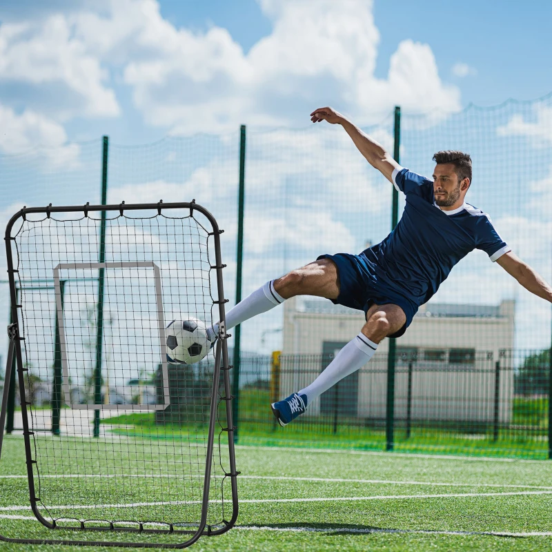 Soccer player kicking ball toward rebounder net on outdoor field.