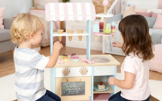 Two kids playing with pastel wooden ice cream and dessert play kitchen set.