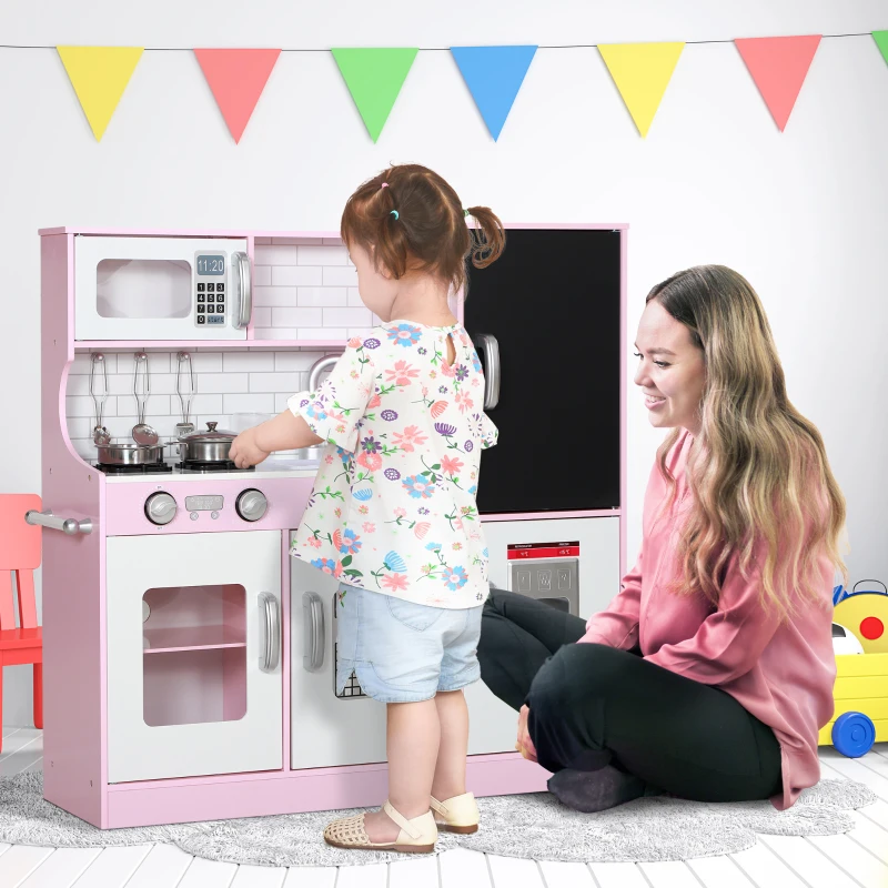 Girl and mother playing with pink toy kitchen featuring chalkboard panel.