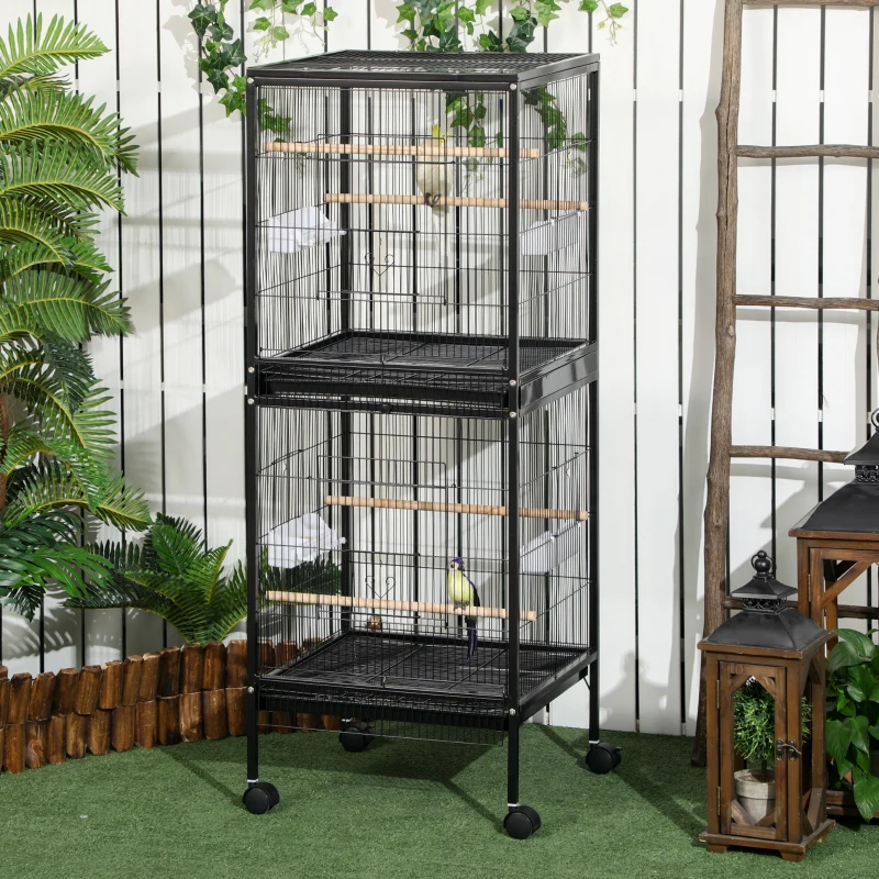 Tall black bird cage with two stacked sections and perches placed outdoors on green grass.