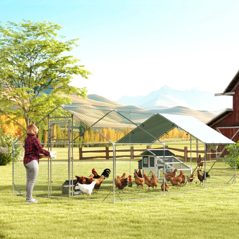 Large outdoor chicken run in countryside with woman feeding hens near barn and mountains.