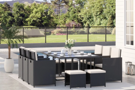 Modern black rattan patio dining set with cream cushions beside pool and garden view.