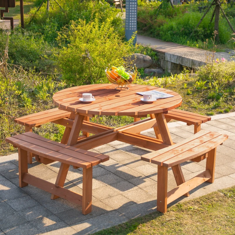 Round wooden picnic table with benches and fruit bowl in sunny garden.