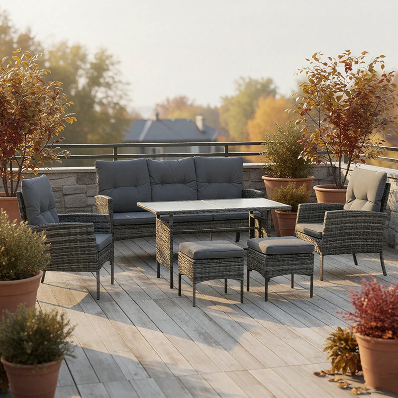 Grey rattan patio furniture set with cushions on rooftop deck surrounded by plants.