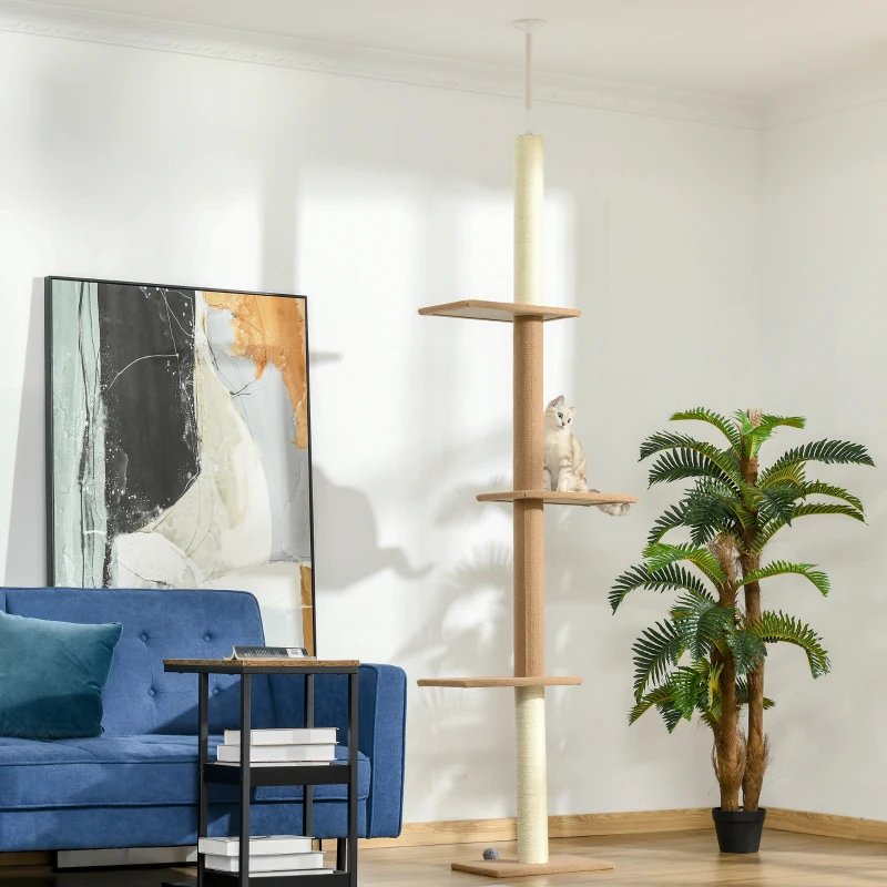 Cat perched on beige floor-to-ceiling tower beside blue sofa and plant.