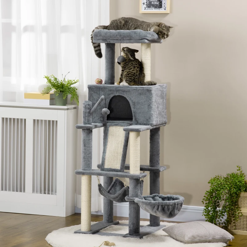 Two cats climbing multi-level grey tower beside green wall.