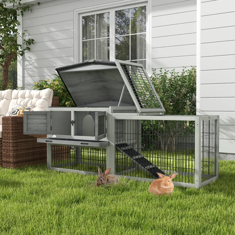 Grey wooden rabbit hutch with open roof and run area, two bunnies on green grass.
