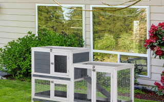 Modern two-tier grey and white rabbit hutch on garden lawn near house windows.