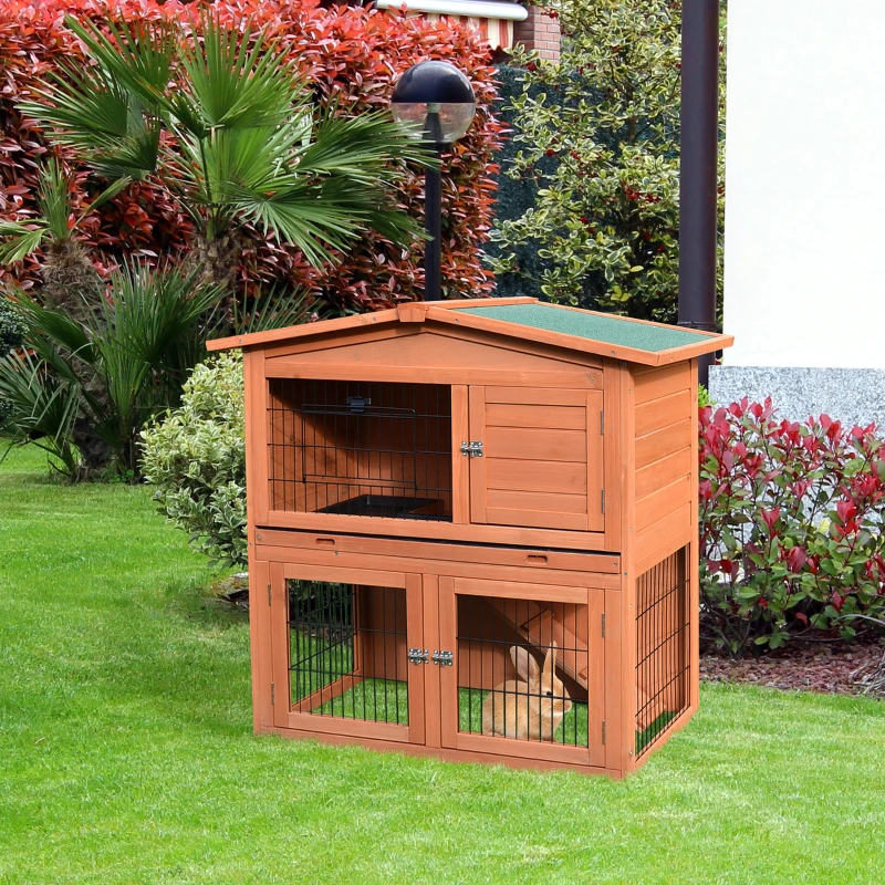Wooden two-level rabbit hutch with ramp and mesh doors placed on green grass.
