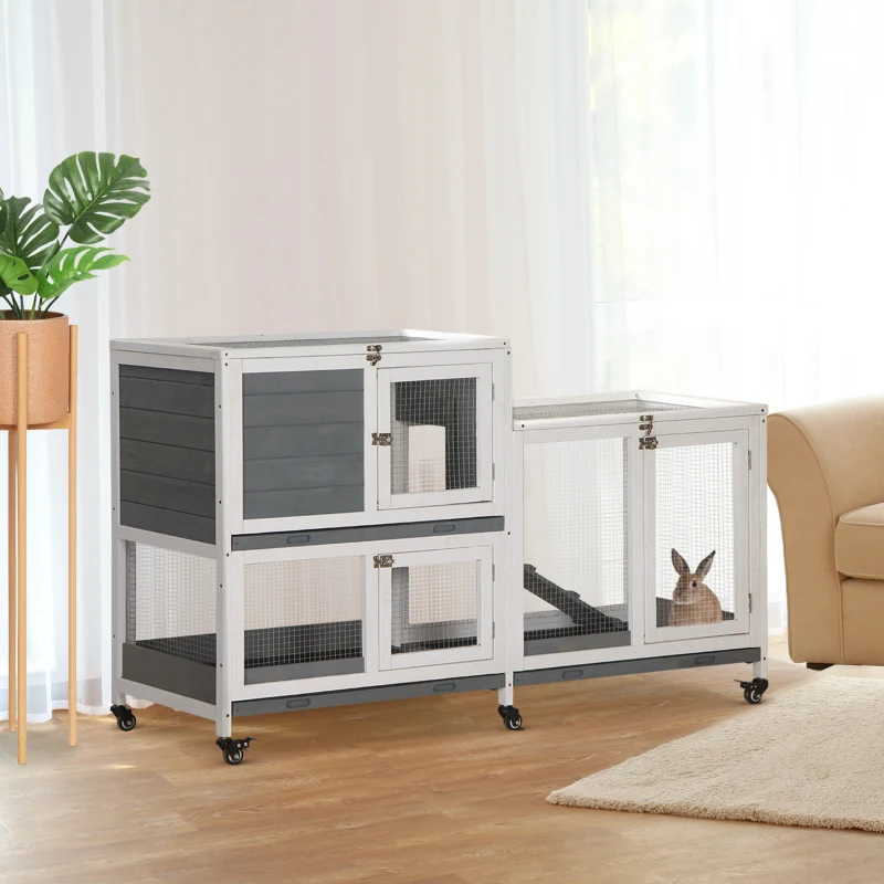 Grey and white two-tier indoor rabbit cage on wooden floor near sofa and houseplant.
