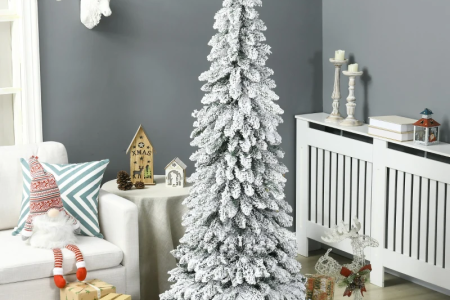 Tall flocked Christmas tree decorated with gifts and ornaments in cosy living room.