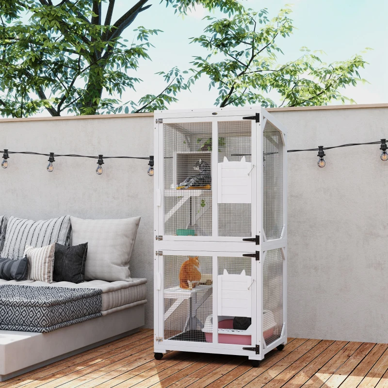 White outdoor cat enclosure with two cats, wheels, and resting boxes on patio deck.