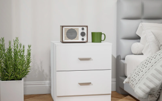 Modern white bedside table beside grey bed with green mug and radio.