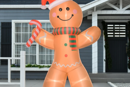 Large gingerbread man inflatable with candy cane outside a grey house in winter.