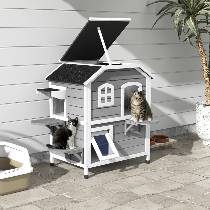 Two cats sitting on multi-level outdoor wooden cat house.
