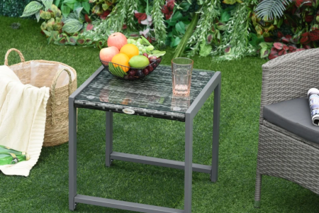 Glass-top rattan table placed outdoors on lawn.