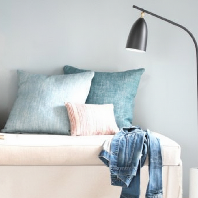 Neutral daybed with layered cushions and jeans draped over edge under reading lamp.