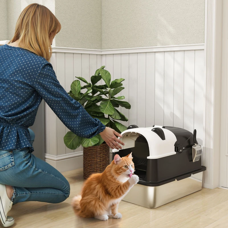 Woman opening black and white covered litter box beside orange cat.