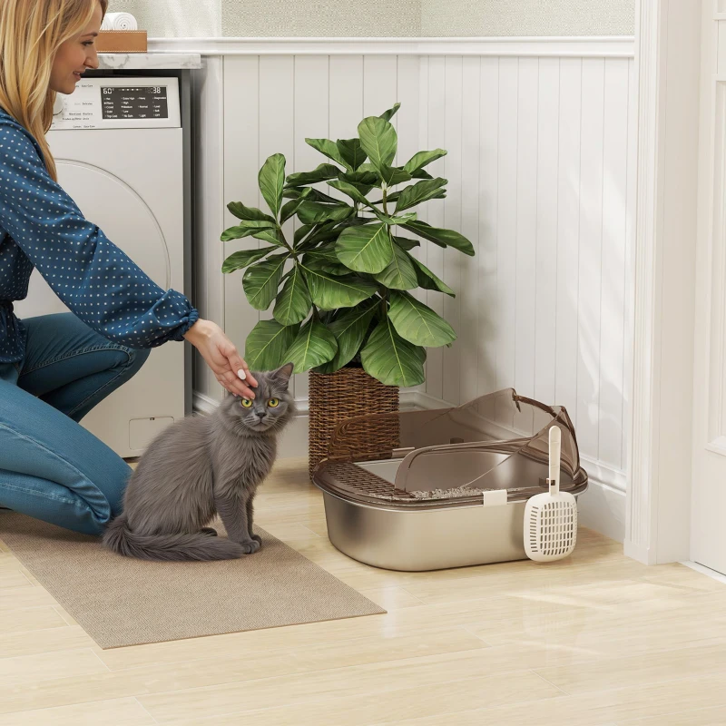 Grey cat sitting beside stainless litter box as woman pets it.