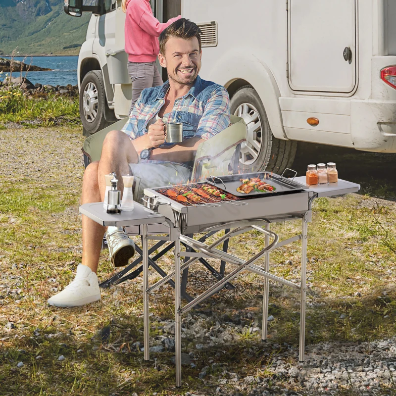 Man grilling skewers on stainless steel Outsunny portable charcoal smoker near camper.