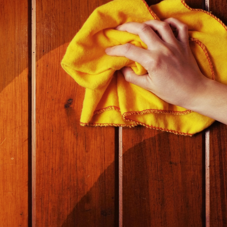 Person polishing glossy wood surface using yellow cloth for restored shine