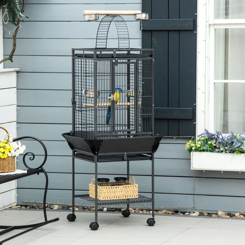 Black bird cage on wheeled stand placed outdoors.