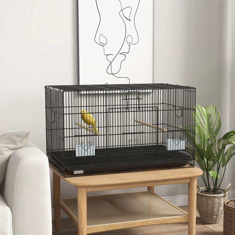 Wide black bird cage with yellow bird on wooden table.