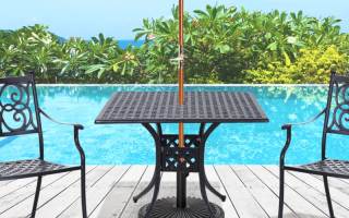 A black cast aluminum patio table with an umbrella hole placed beside two chairs near a pool.