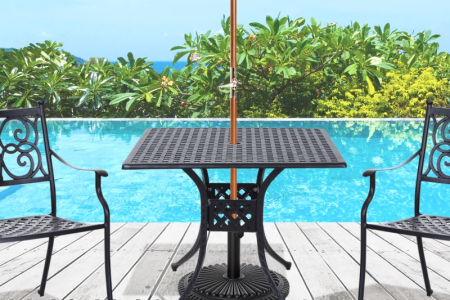A black cast aluminum patio table with an umbrella hole placed beside two chairs near a pool.