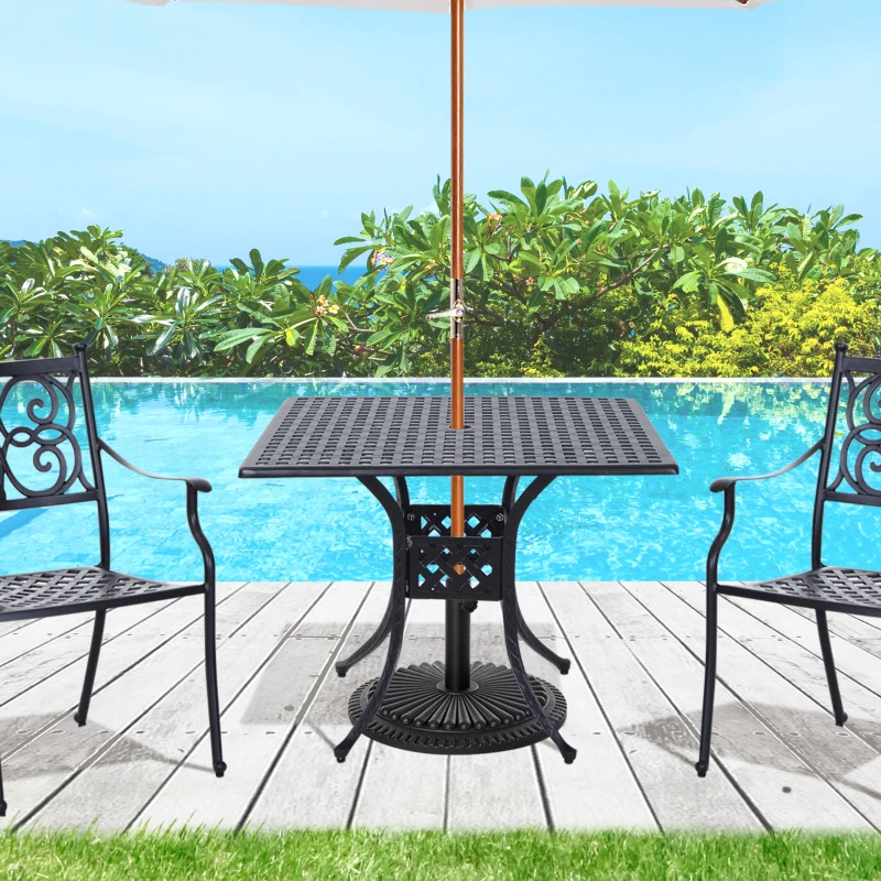 A black cast aluminum patio table with an umbrella hole placed beside two chairs near a pool.