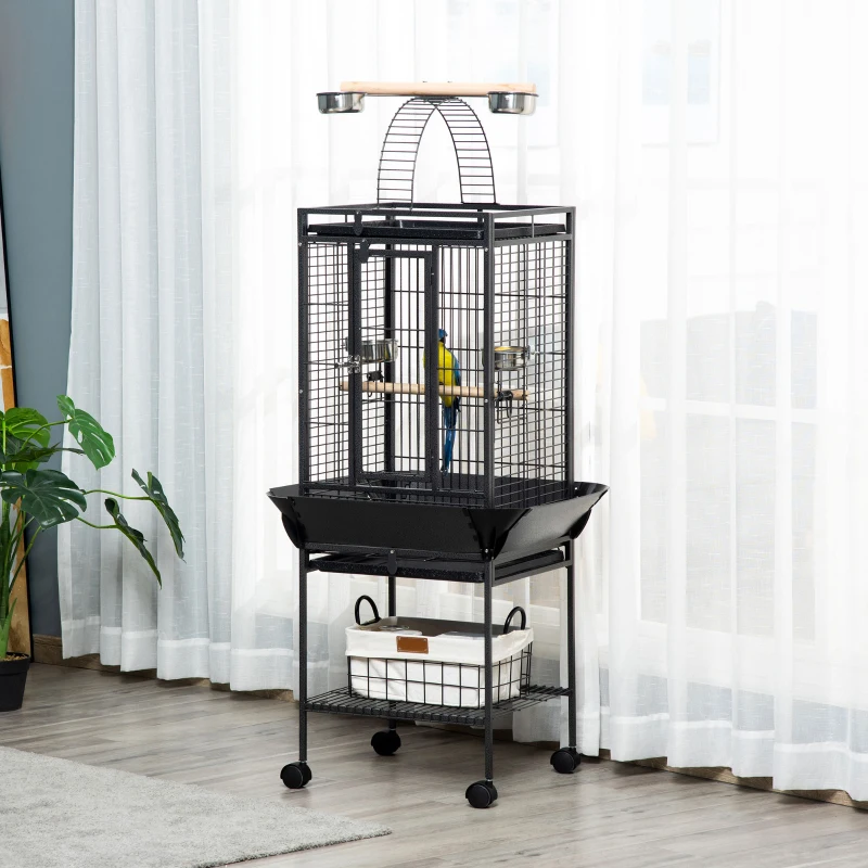 Tall indoor bird cage with a parrot perched inside, set near bright window curtains.