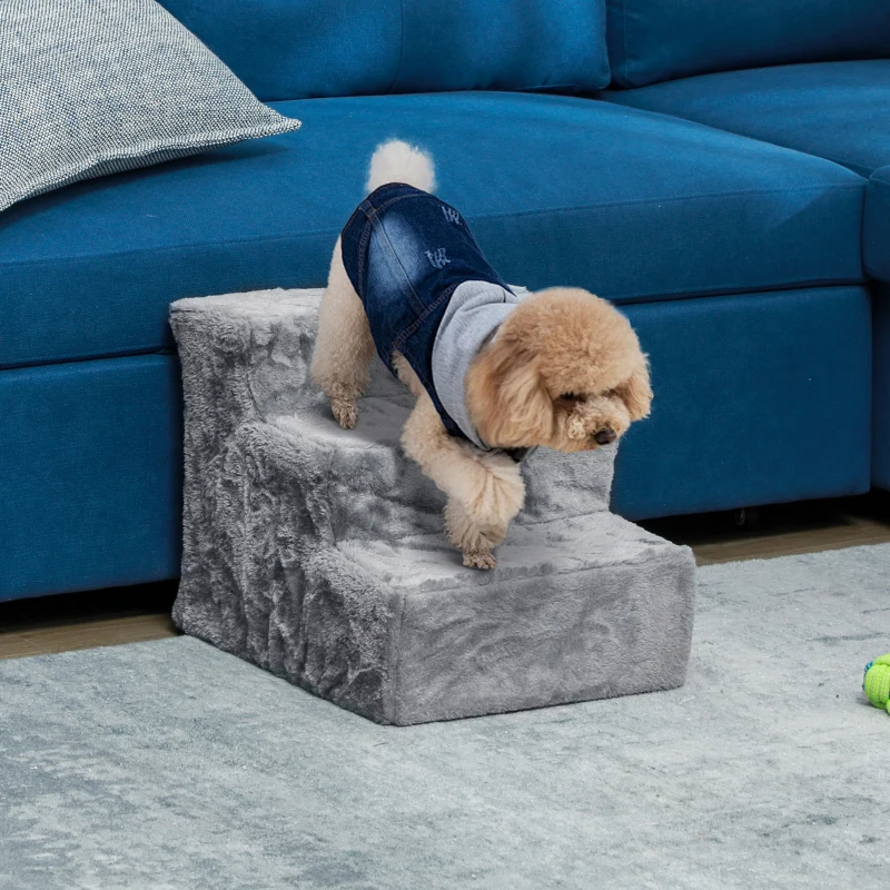   The dog uses soft grey pet stairs to climb down from a blue sofa in a living room.