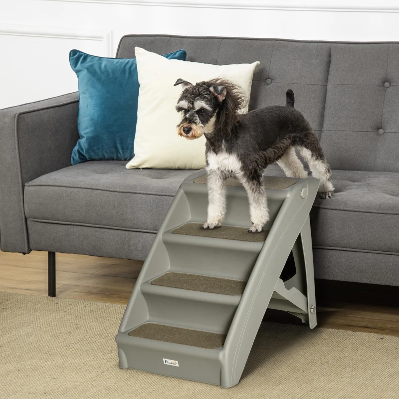   A small dog standing on foldable plastic pet stairs beside a grey sofa in a cozy room.