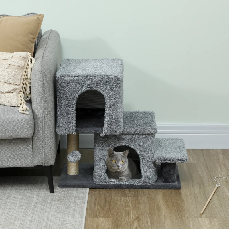   Grey cat resting inside multi-level cat condo with steps and scratching post beside sofa.