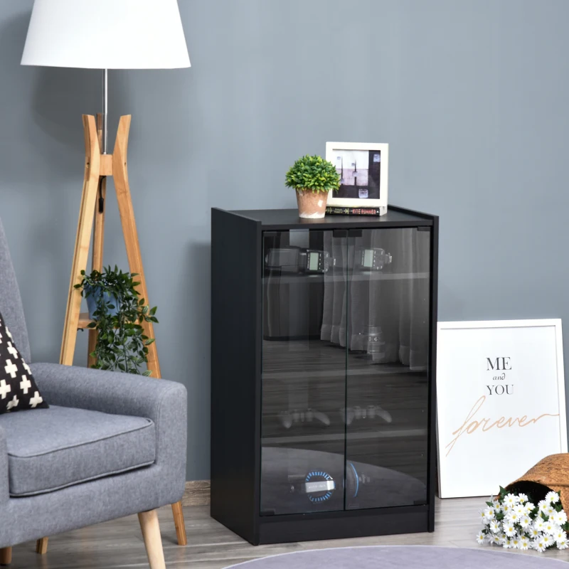 Black glass-door media stand holding consoles and décor beside a grey armchair and floor lamp