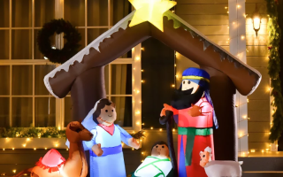 Lighted nativity inflatable with figures under star-topped stable in front-yard Christmas décor.