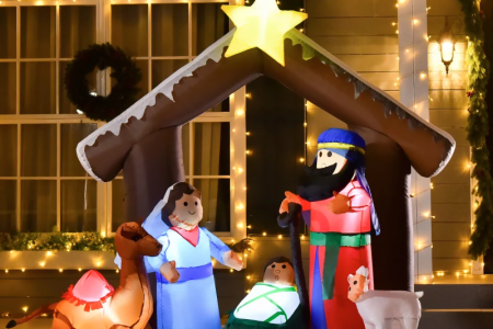 Lighted nativity inflatable with figures under star-topped stable in front-yard Christmas décor.