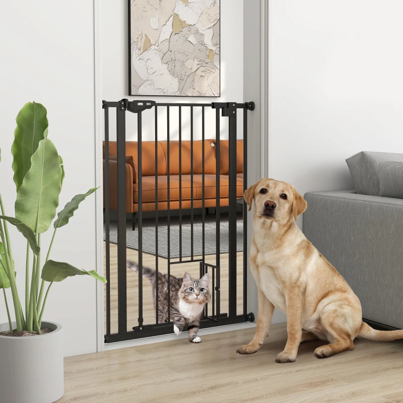 Modern black pressure-mounted dog gate with cat door beside dog and kitten.