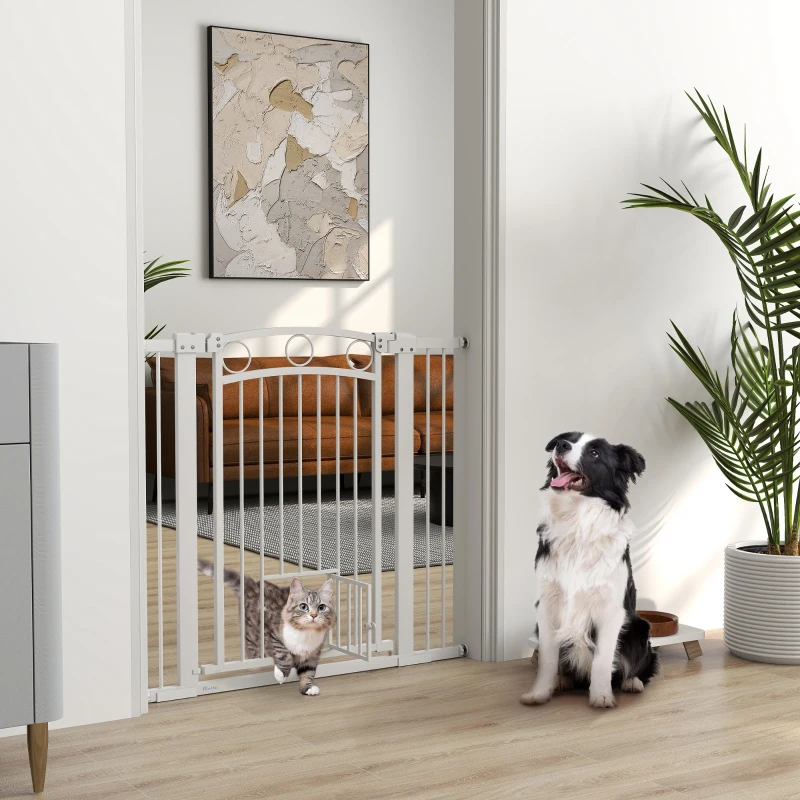 Tall white pressure-mounted dog gate with small cat door separating pets indoors.