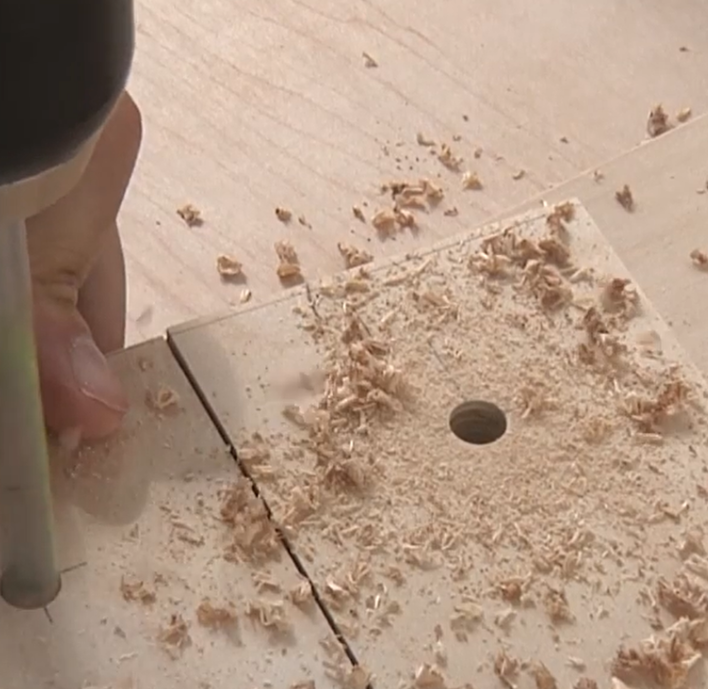 Drilling a clean round hole through plywood on a work table.