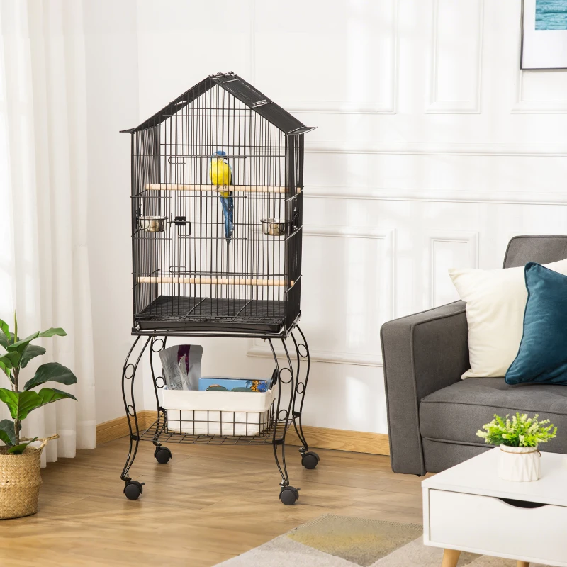 Black bird cage with house-style roof and curved legs holding yellow parrot indoors.