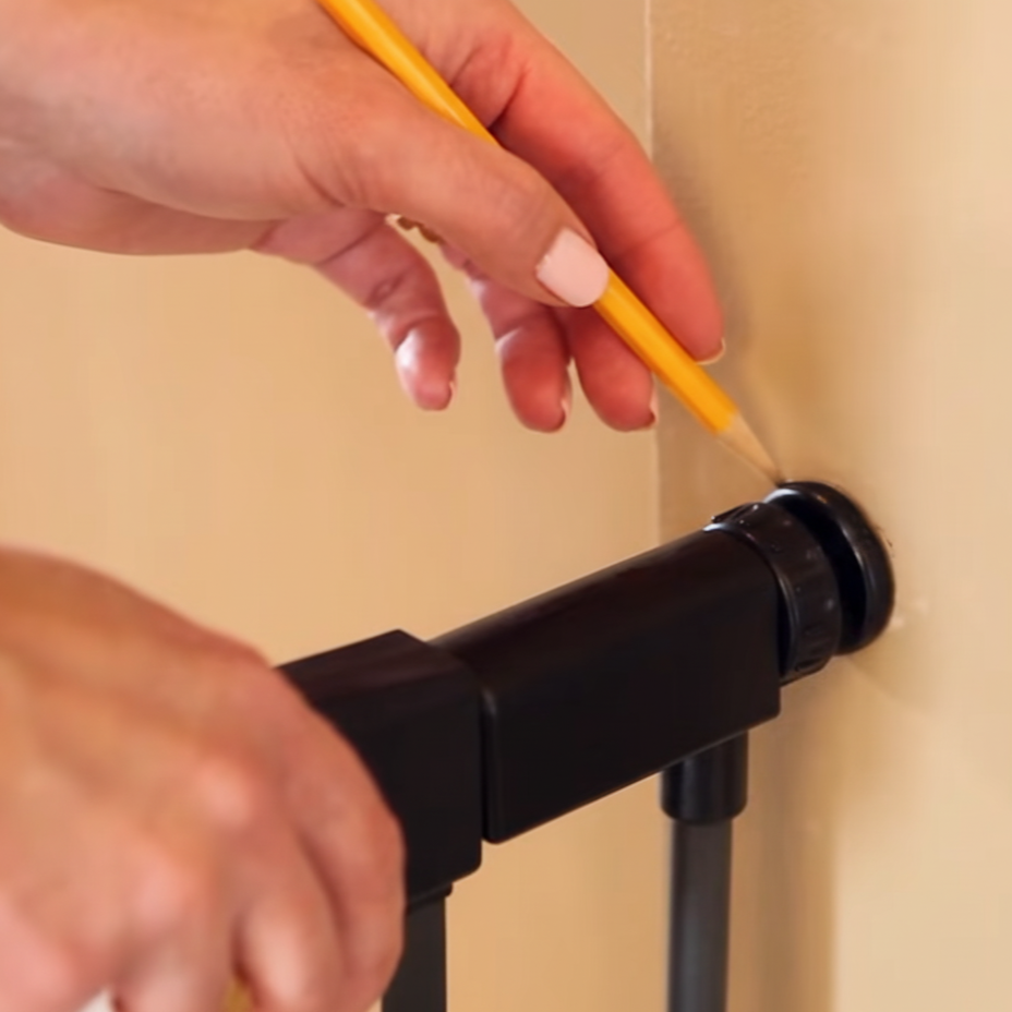 Marking wall with a pencil to align mounting cups for pet gate installation.